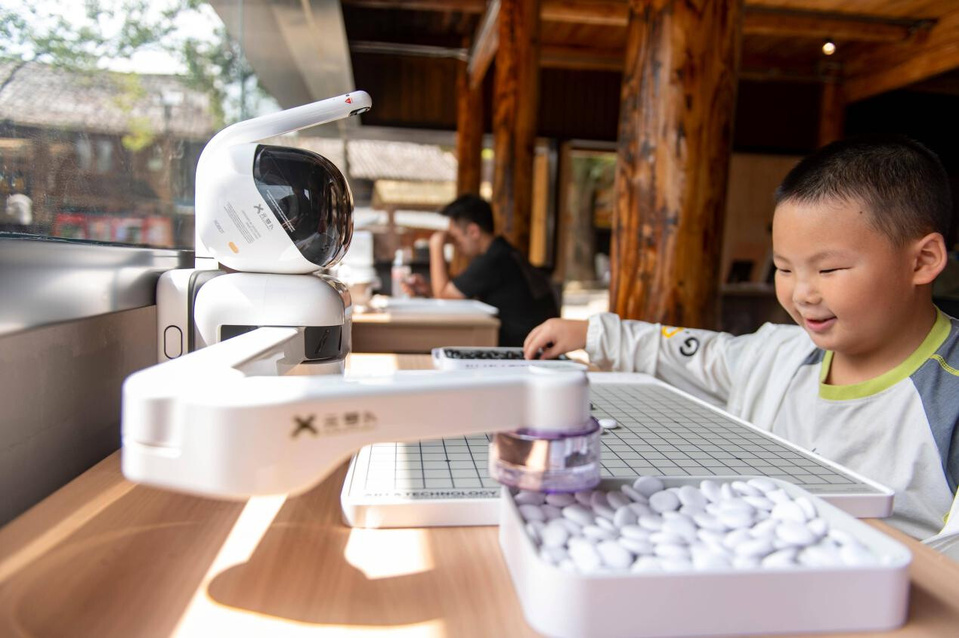 A boy plays go with an AI-powered robot at a tourist site in Congjiang county, southwest China's Guizhou province, Aug. 9, 2025. (Photo/Wu Dejun)