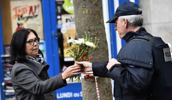Une femme demandant à un policier de déposer un bouquet de fleurs sur la rue de Charonne. AFP/LOIC VENANC