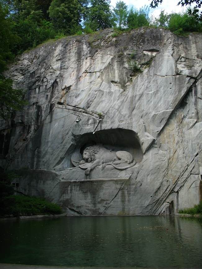 Le Lion de Lucerne mortellement blessé.  Lion mourant avec la mention "à la loyauté et à la bravoure des Suisses", transpercé par une lance couvrant un bouclier portant la fleur de lys de la monarchie française et avec un autre bouclier portant les armoiries de la Suisse. Dessin du sculpteur danois Bertel Thorvaldsen, taillé par Lukas Ahorn dans une ancienne falaise de grès de Lucerne en Suisse. Dimension : 10 mètres de long et 6 mètres de haut © Photo : Andrew Bossi.